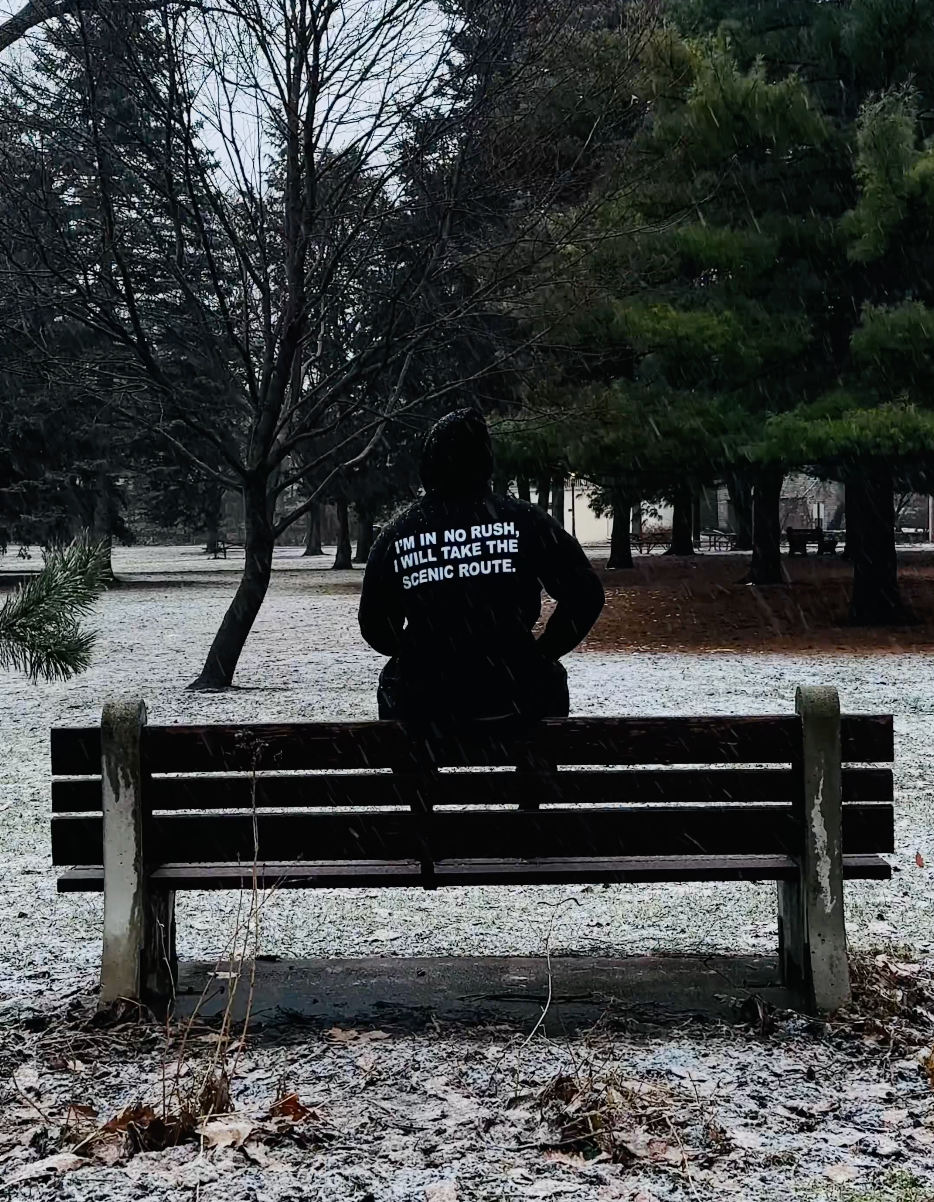 Someone in the black Entry 001 hoodie sitting alone on a park bench in the snow.